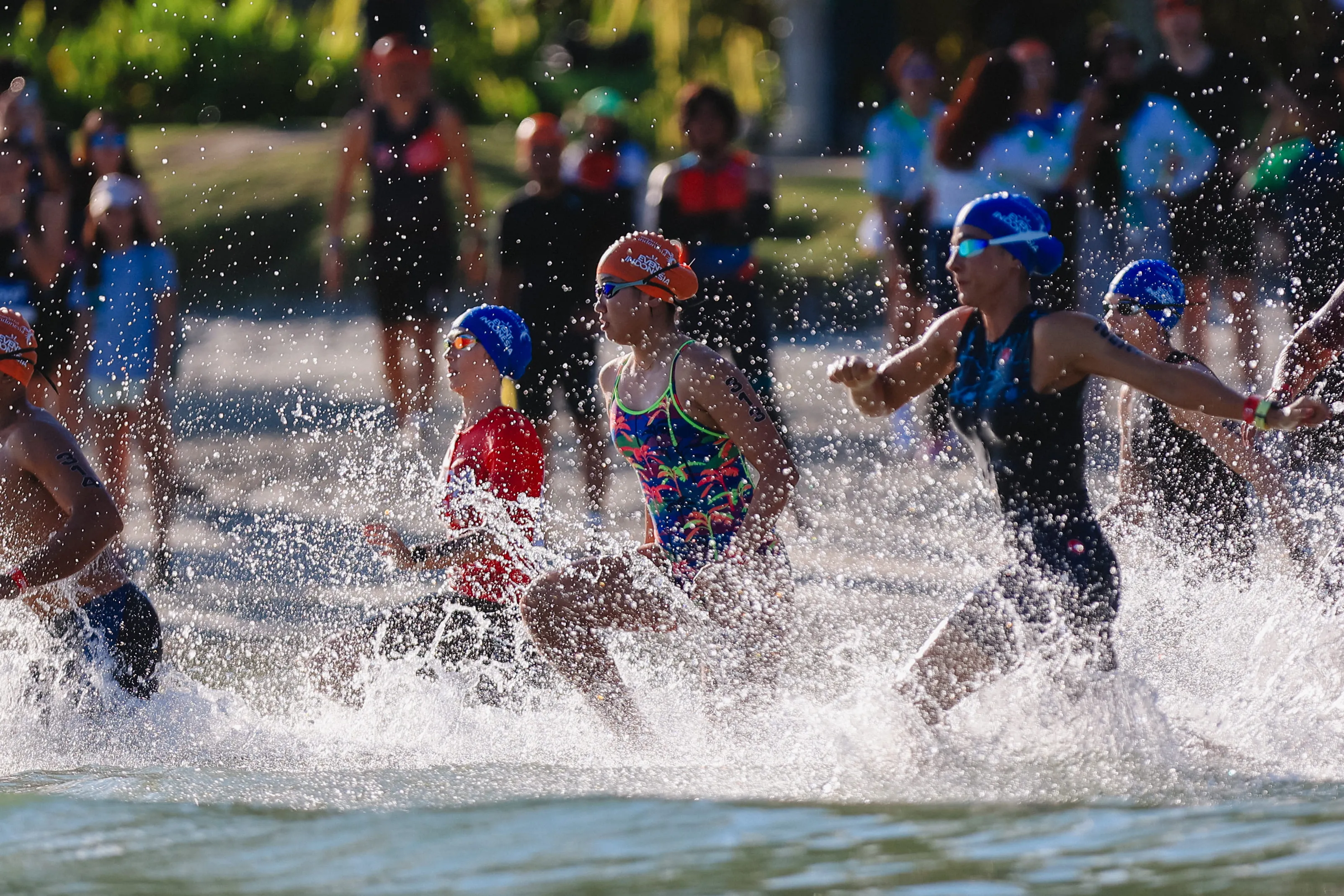A triathlete swimming in clear turquoise water beside Bintan's palm-lined shoreline at sunrise